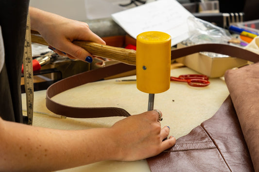 A leather crafting artist is holding a yellow poly mallet to adjust the closure and placement of a brown kangaroo leather bell.